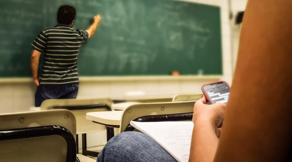 boring classroom where a student is searching on her cellphone for what is the best online business for beginners 1